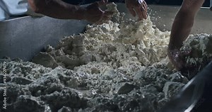 Super slow motion close up of artisan cheesemakers mixing with their hands fresh bio eco milk mass during traditional cheese making process at cheese production creamery dairy factory at 1000 fps.