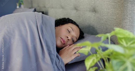 African American woman waking from eyelid flutter, opening eyes, turning head on bed in gray duvet