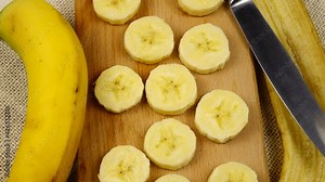 Unpeeled banana, banana peel, banana slices on a cutting board and a table knife lie on the table, rotation