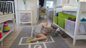 Cute 3-year-old child with a handheld vacuum cleaner cleaning floors in room