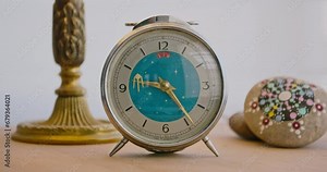A classic mechanical alarm clock with a rotating second hand in the shape of a kite, on a decorated table, tells the time
