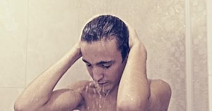 Young man relaxes in the shower. Teenager takes shower in the bathroom. Man washes under stream of warm water. European human rinses hair with water. Real time.