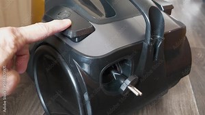 Vacuum cleaner cord retractor. Mechanism or system for winding the cord in vacuum cleaner. Man presses button and electric cable winds up inside vacuum cleaner. Vacuum cleaner cord winding mechanism