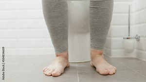 Low Section Of Woman Sitting On Toilet Bowl In Bathroom.