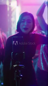 Vertical video: Woman filming vlog for social media, using smartphone at nightclub on dance floor. Young adult recording fun video of friends dancing and partying together, entertainment. Handheld