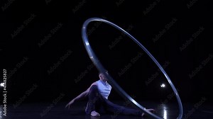 Male muscular acrobat shows difficult tricks for a balance and concentration while spinning on a Cyr wheel