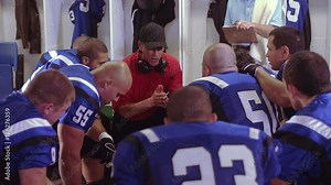 Football players sit in a circle in the locker room and coach gives a speech