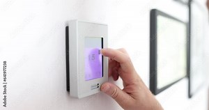 Person hand changes temperature in apartment using wall control panel. Owner wants to cool off spacious residence house during hot day slow motion