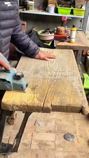 Smoothing an old wooden board using a power hand planer to remove the rough surface in a workshop
