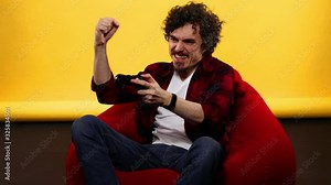 Nerdy gamer with controller on yellow background. Man with curly hair