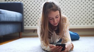 Tween girl with smartphone lying on the carpet.