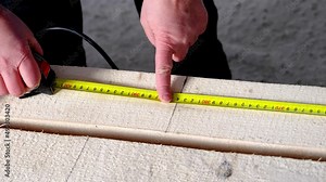 Measuring yellow tape measure scale with centimeters on wooden boards for marking the place of cutting. Lumber, house construction, carpentry. Slow Motion
