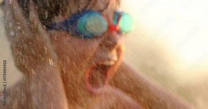Child screaming from the top of his lungs while emerged by water in slow-motion 60fps and 4k resolution clip. Cinematic scene of young boy screaming and covering ears with hands while water sprinkles