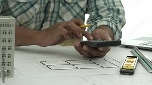 Close up Asian individual architect or engineer holding building scale model of multi-story building. design or review of architectural plans laid out on work surface in front of them.