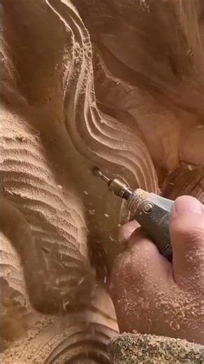 Carving intricate wavy patterns on a large wooden block using a rotary tool for art projects
