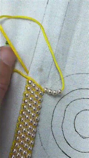 sewing beads onto fabric using a needle and yellow thread for an intricate handicraft project
