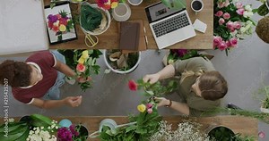 young florist business woman in startup flower shop making beautiful bouquet working together with colleague in successful store overhead