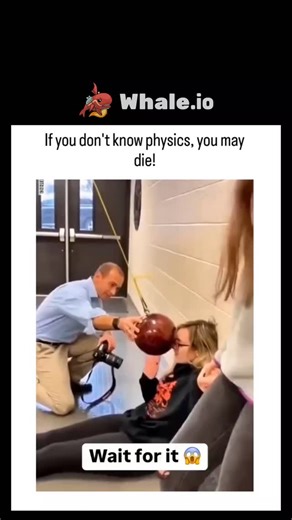Explains Cosmos on Instagram: "The post shares a viral video showing a simple but powerful pendulum physics experiment. In the clip, a girl lies calmly under a hanging ball that is released from rest. Because of energy conservation, the ball swings back but stops just short of her face, proving the concept in a safe and dramatic way. The video then contrasts this with a man who pushes the ball before letting it go. By adding extra force, he injects more energy into the system, causing the pendul