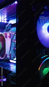 Vertical video. Dark room with a gaming computer with a transparent side panel revealing internal components with RGB lighting and a monitor in the distance.