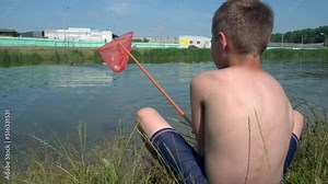 A little boy with a butterfly net catches fry in the lake.