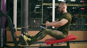 Shot in 4k: side view of a man in gym doing pulls back with weight. Attractive man is training back muscles using exercise cable machine for body mass. Workout and bodybuilding sport concept