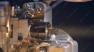close-up view of a vintage film projector playing a movie in a movie theater. The reel of film spins and a beam of light pierces the darkness.