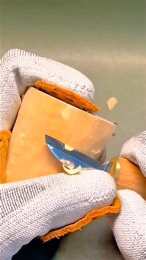 Whittling a small wooden block using a sharp carving knife while wearing protective safety gloves