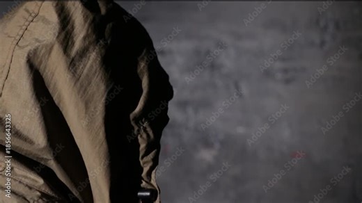 Anonymous hooded hacker with back to camera during police interrogation in a dark station room. Cybercrime investigation, law enforcement questioning, secrecy