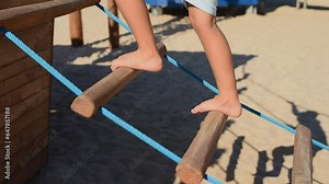 Bare children's feet climb a rope ladder in summer on a wooden eco-friendly playground