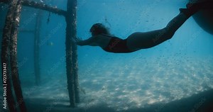 Woman freediver swimming underwater in blue sea. Female freediving with fins under the pier