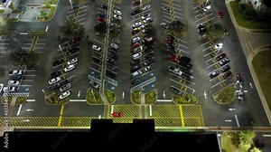 View from above of many parked cars on illuminaded parking lot with lines and markings for parking places and directions. Place for vehicles in front of a shopping mall center