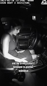 The officer’s attention is drawn to the interior of a vehicle during a traffic stop. Movement inside reveals an object that does not match the surrounding items. The officer shifts position closer to the window. The angle exposes more of the front seating area. A firearm becomes visible inside the vehicle. It is positioned within reach of a seated woman. The officer pauses and adjusts stance to confirm the view. The placement remains unchanged as observed. The camera captures the firearm clearly