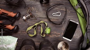 Hiking accessories. Boots, backpack, sunglasses, photo camera, map, smartphone, flashlight and others. Top view.