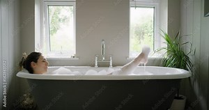 Beautiful Woman lying in bathtub enjoying relaxing bubble bath experiencing mindfulness lifestyle with real natural body care authentic homemade spa treatment