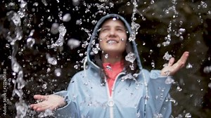 young woman stands under the water of a waterfall. Close-up face, slow motion