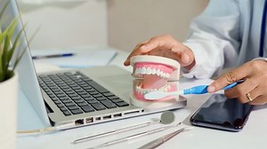 Dentist teaching explaining how to brush teeth correctly to patient after treatments on doctor desk with laptop computer, tutorial showing instructional brushing movements teeth clean dental hygiene