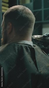 Dark dimly lit artistic shot with a trimmer haircut in a barbershop. A gloved craftsman using trimmer to align the length of the customer hair in the chair. Vertical shot.