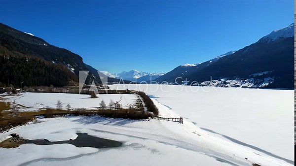 Lake Reschen - Vinschgau, South Tyrol - Aerial view of the frozen white lake with a view of the Ortler mountain range
