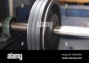 Close-up of a rotating industrial pulley system with dual V-belts on a polished shaft, showcasing motion and mechanical power transmission in a factory environment.