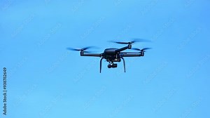 Person control flying drone with video camera. Modern technology. Air copter robot fly against blue sky above field. Nature background. Aerial Multicopter, rotating propeller. Man launches cam drone.