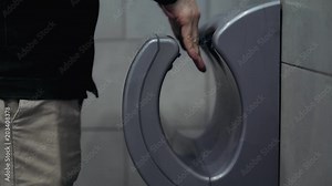 Man dries wet hand in modern vertical hand dryer in public restroom WC airport terminal