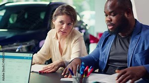 Customers in showroom completing credit application and financing paperwork after deciding to purchase new car. Salesman in dealership discussing financing options with clients, camera A