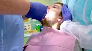 Team of dental surgeons performs surgery on teeth. in a modern clinic. Young dentist. Teamwork. Tooth doctor orthodontist surgeon doing medical operation on root canals. Stomatology office.