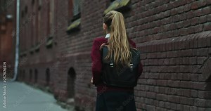 Back view on the Caucasian schoolgirl in the uniform and with a bag walking the street after classes at school. Close up. Rear.