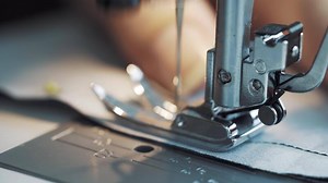 Close-up of work of sewing machine mechanisms. Women's fingers move fabric for stitching and pull needles out of material. Making clothes at home. Dressmaker's workshop.
