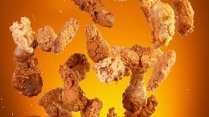 Super slow motion of flying fried chicken pieces hitting in the air, isolated on golden background. Filmed on high speed cinema camera, 1000fps. Speed ramp effect.