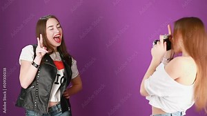 Two hipster girls make photo with old camera in studio on purple background