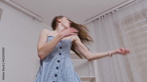 Young woman dances wildly in slow motion, hair flying and dress swirling, radiating energy and joy in a bright living room