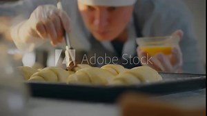 Recipe. A chef dressed in uniform brushes dough products in an industrial kitchen. Cinematic shot of a European worker working with puff pastry adheres to the traditions of preparing breakfast, bakery