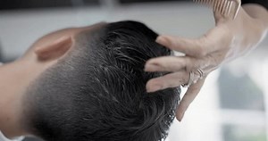 Barber doing a haircut to male client in barbershop close up. Close up of a Barber scissor cutting a young mans hair.